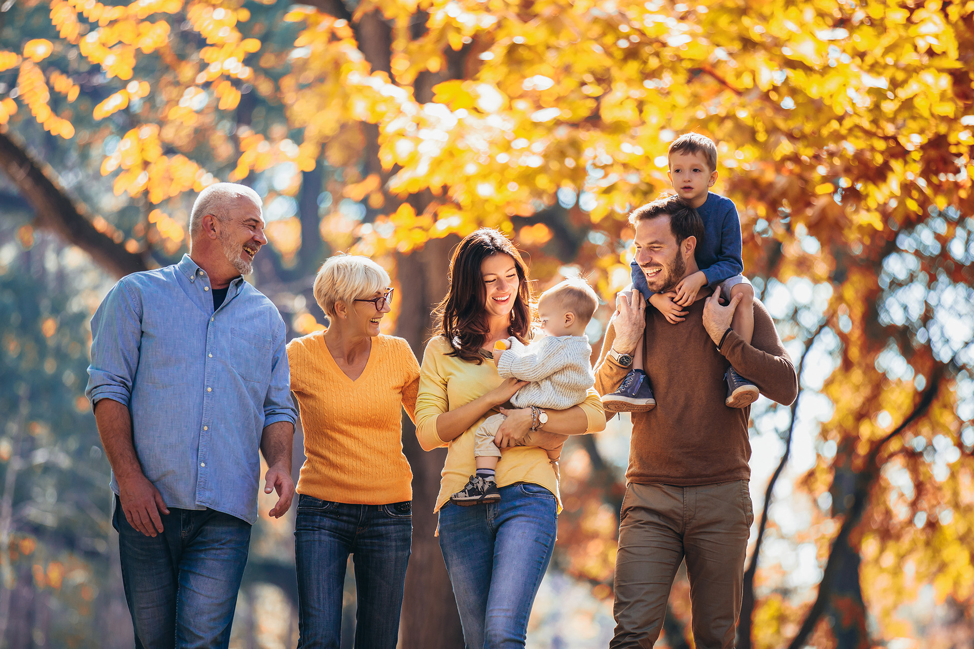 A family walking outside together with trees in autumn colours in the background.