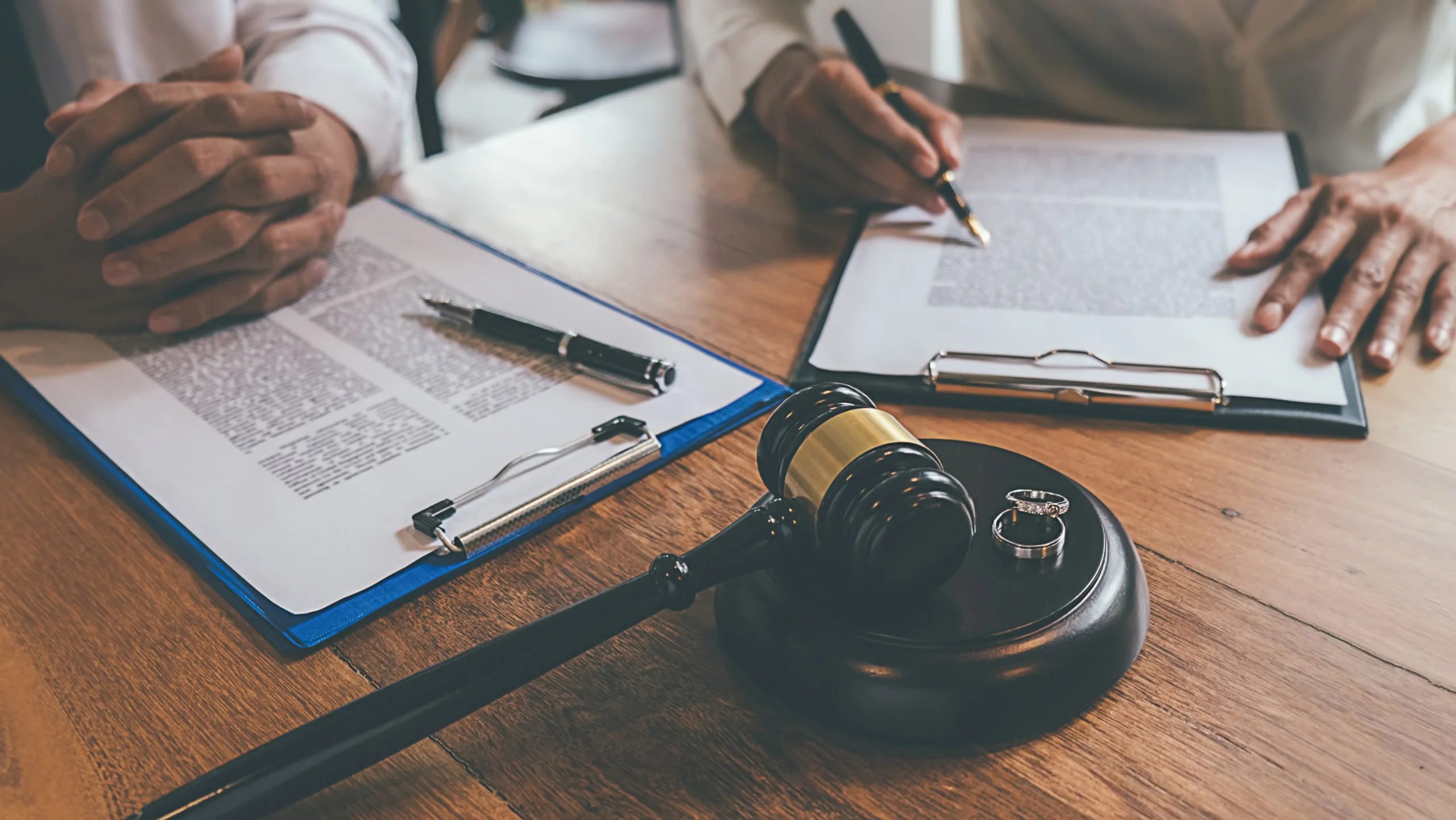 Two people sign divorce papers in front of a gavel