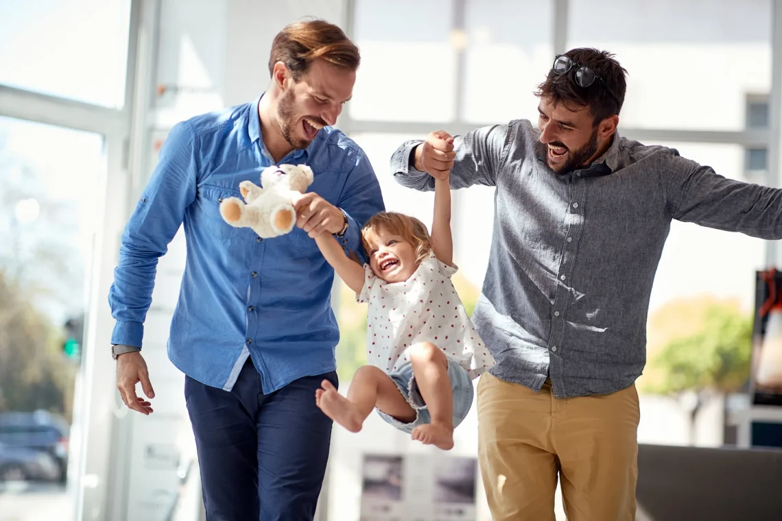 Two smiling men holding hands with their child.