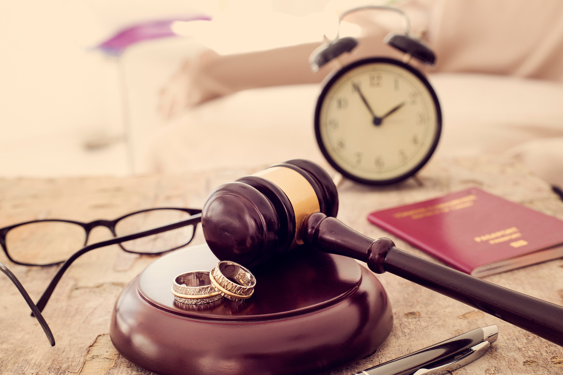 A gavel on a desk with two wedding rings, glasses, a clock, a pen, and a passport. The scene conveys themes of legal decisions and divorce.