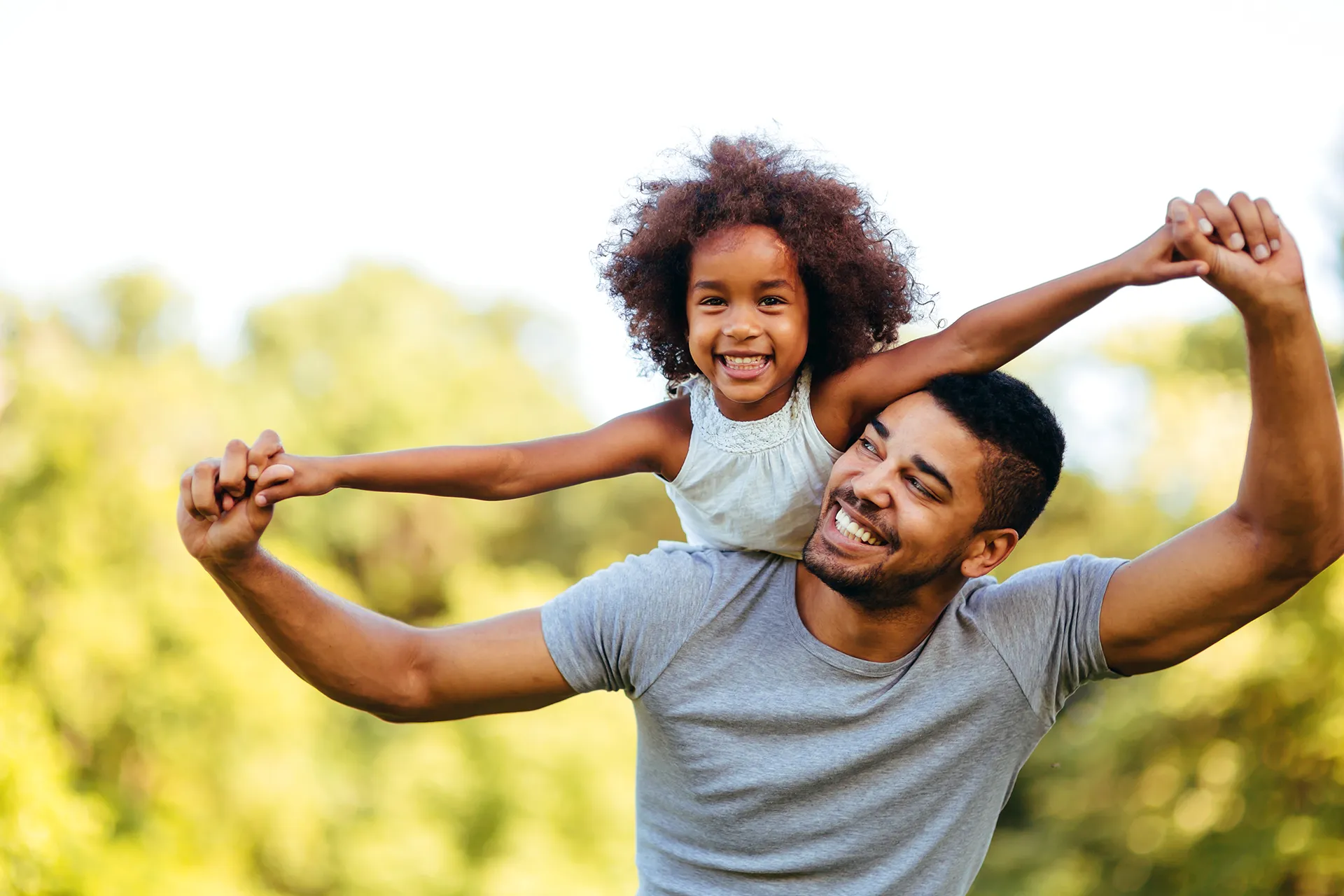 A happy father holding his smiling daughter on his shoulders.