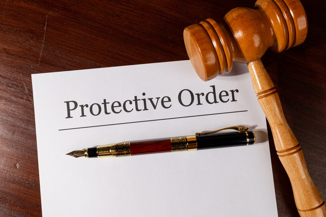 A document titled "Protective Order" resting on a wooden surface beside a judge's gavel and a fountain pen.