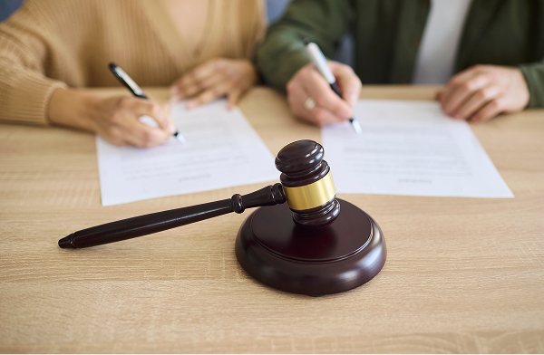 Gavel and divorce documents on a desk with a couple signing paperwork in the background.